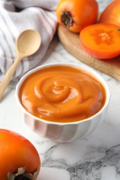 Photo of Delicious persimmon jam and fresh fruits on white marble table