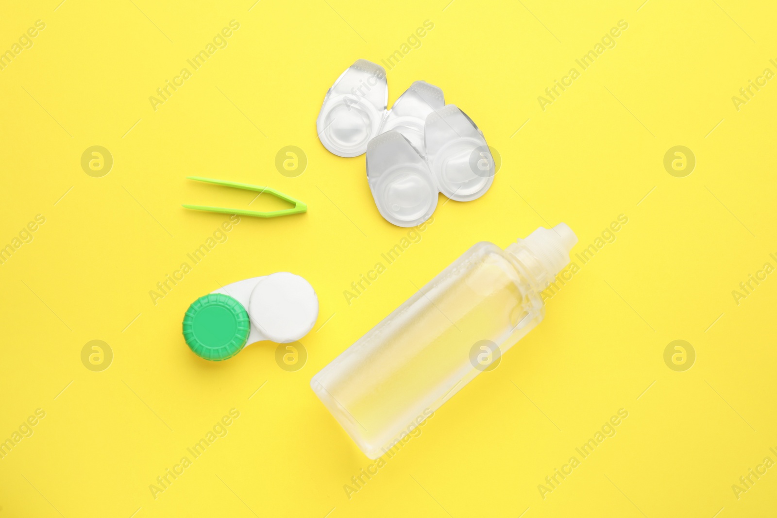 Photo of Packages with contact lenses, case, tweezers and drops on yellow background, flat lay