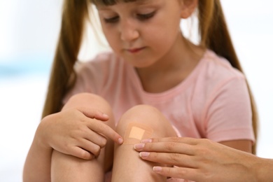Photo of Woman applying plaster on girl's knee, closeup view