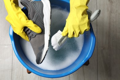 Photo of Woman with gloves and brush cleaning stylish sneakers in wash basin, top view