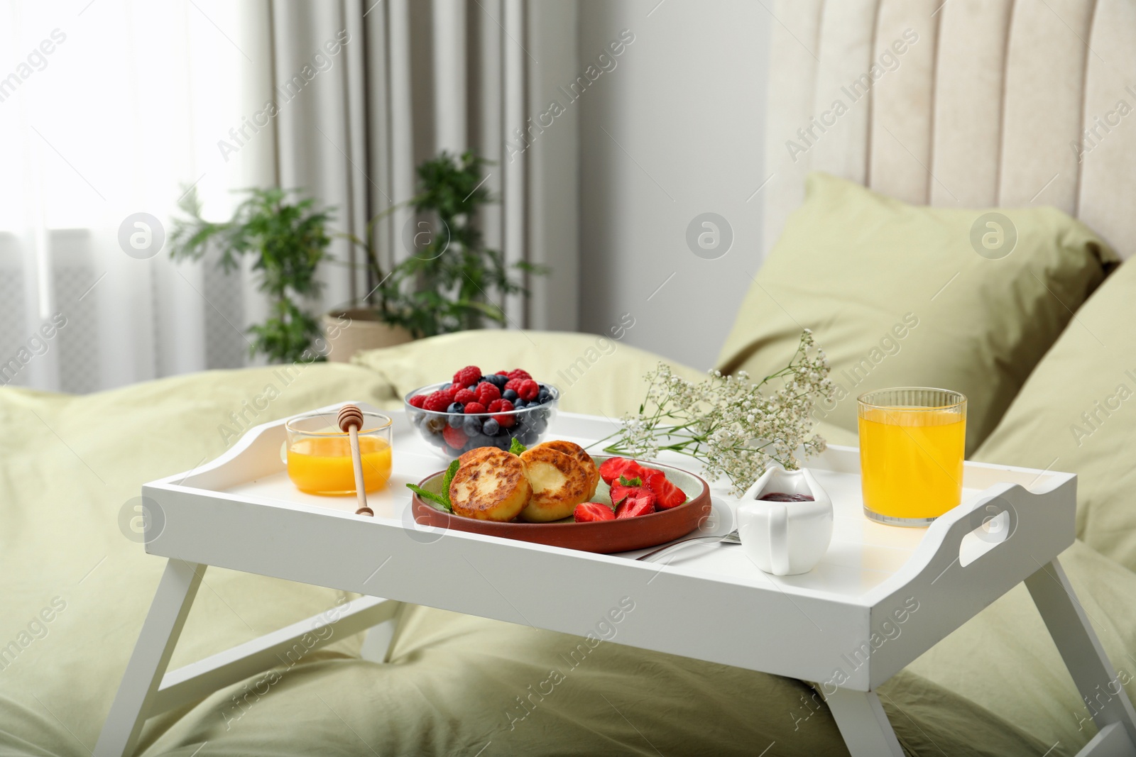 Photo of Tasty breakfast served in bedroom. Cottage cheese pancakes with fresh berries and mint on white tray