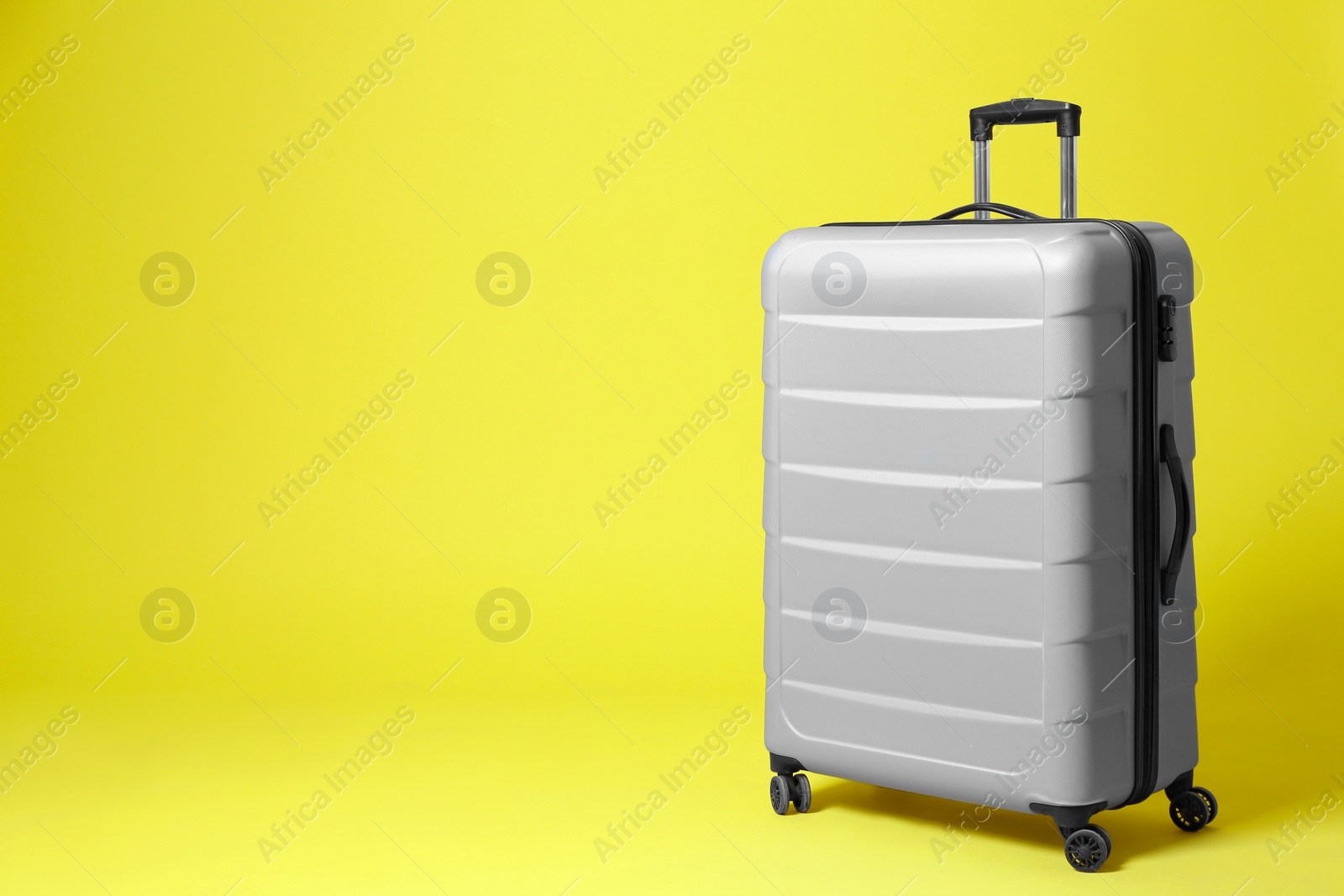 Photo of Stylish grey suitcase on yellow background. Space for text