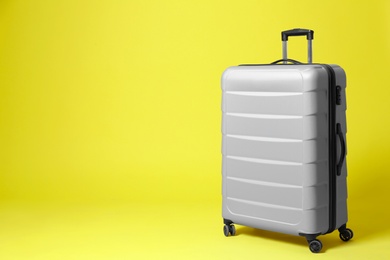 Photo of Stylish grey suitcase on yellow background. Space for text