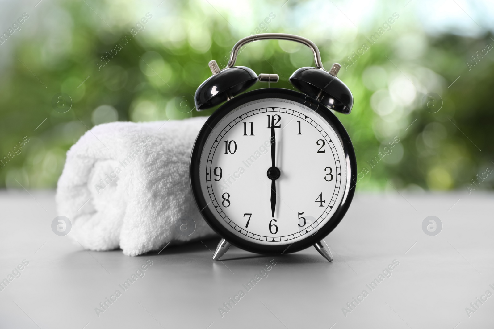 Photo of Alarm clock and towel on grey table against blurred background. Morning exercise