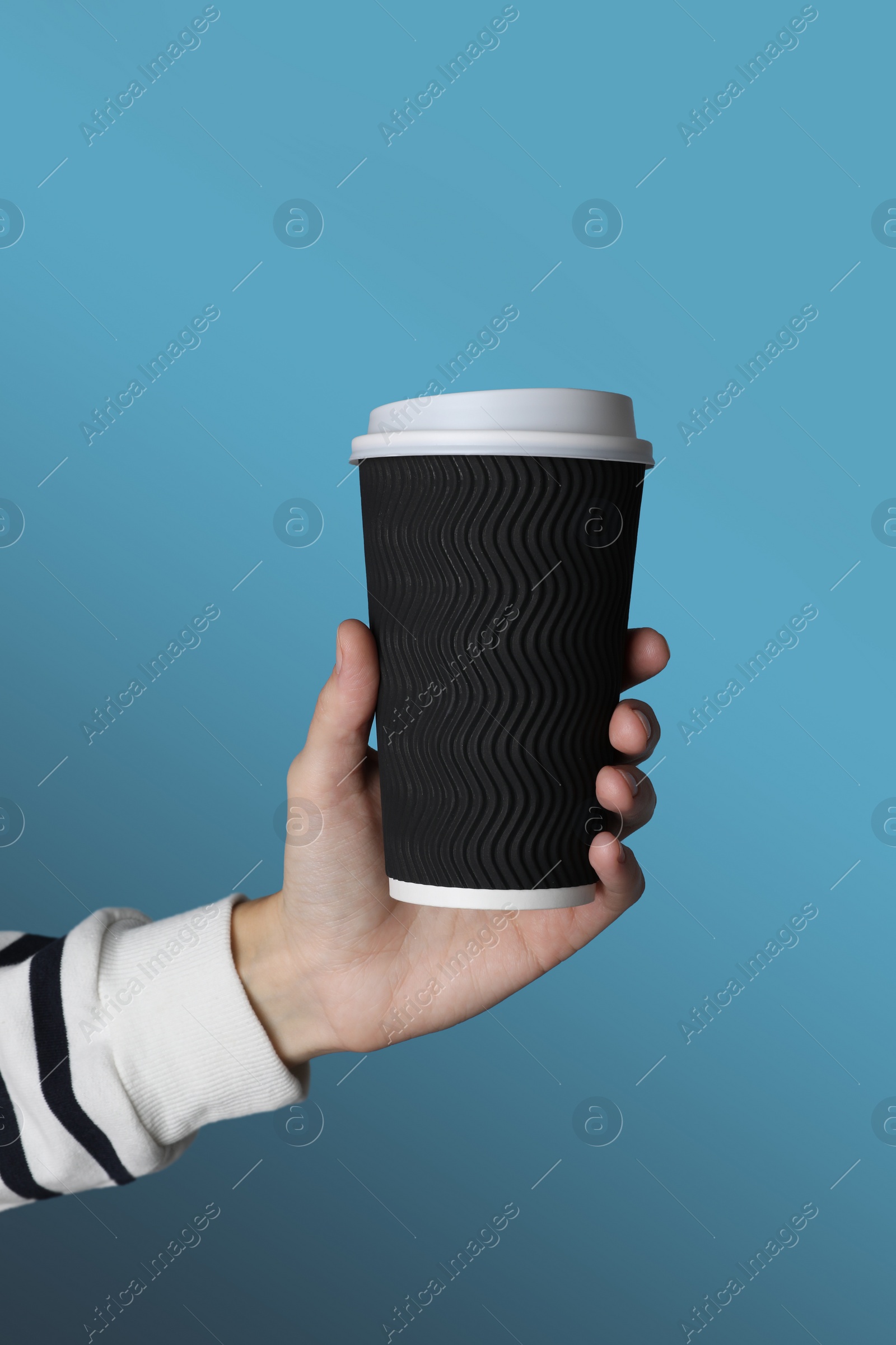 Photo of Woman holding takeaway paper coffee cup on blue background, closeup