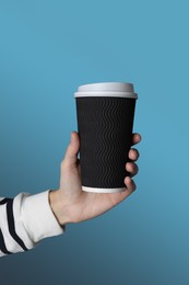 Woman holding takeaway paper coffee cup on blue background, closeup