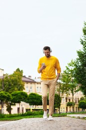 Photo of Handsome man with smartphone and headphones walking on city street