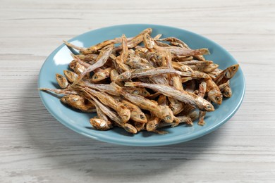 Photo of Plate of tasty dried anchovies on white wooden table, closeup