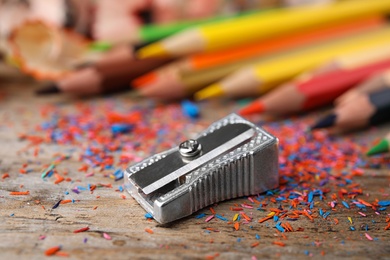 Photo of Color pencils, sharpener and shavings on wooden table, closeup
