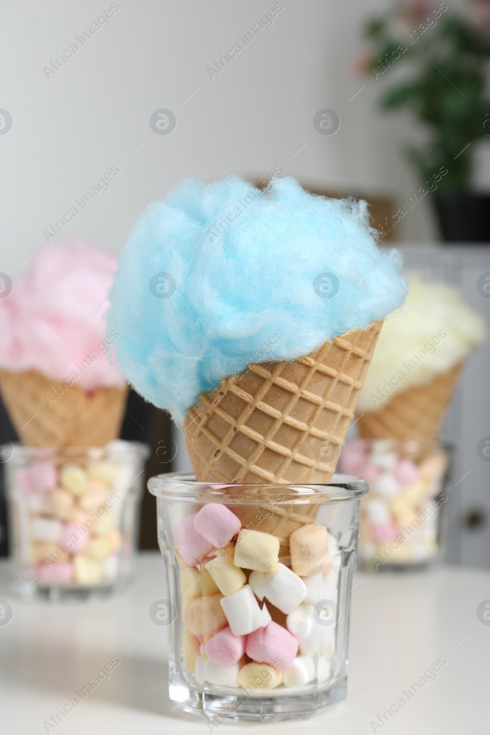 Photo of Sweet cotton candies in waffle cones and marshmallows on white table indoors, closeup