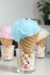 Photo of Sweet cotton candies in waffle cones and marshmallows on white table indoors, closeup