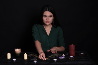 Photo of Soothsayer predicting future with tarot cards at table on black background