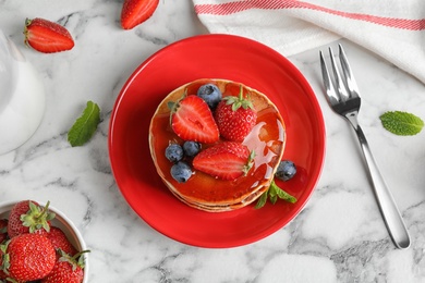 Delicious pancakes with fresh berries and syrup served on white marble table, flat lay