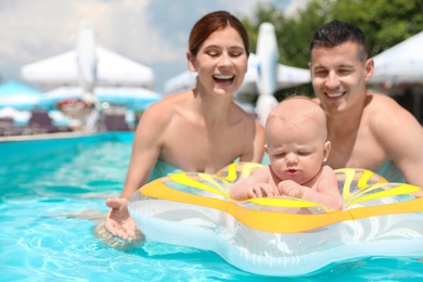 Happy parents with little baby in swimming pool on sunny day, outdoors