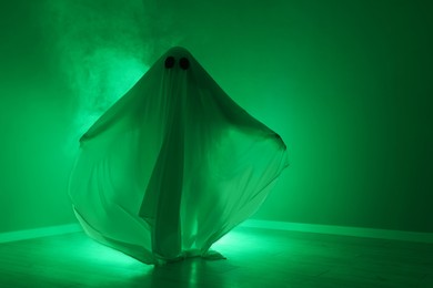 Creepy ghost. Woman covered with sheet in green light, space for text