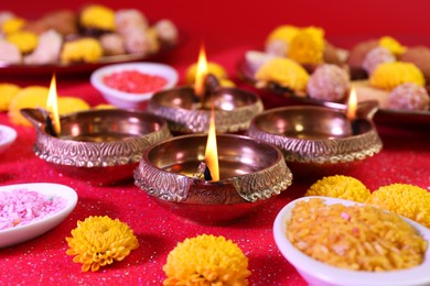Photo of Diwali celebration. Diya lamps, bright rangoli and chrysanthemum flowers on shiny red table, closeup