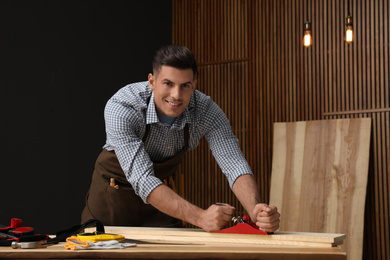 Handsome carpenter working with timber at table indoors
