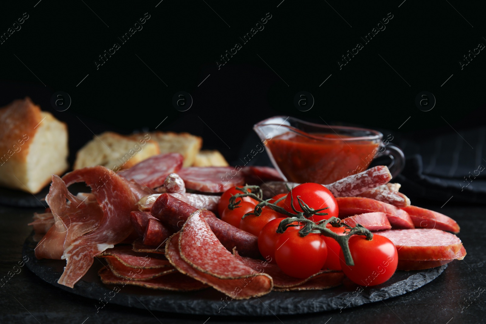 Photo of Different types of sausages with tomatoes served on black table