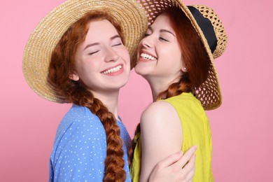 Photo of Portrait of beautiful young redhead sisters in straw hats on pink background