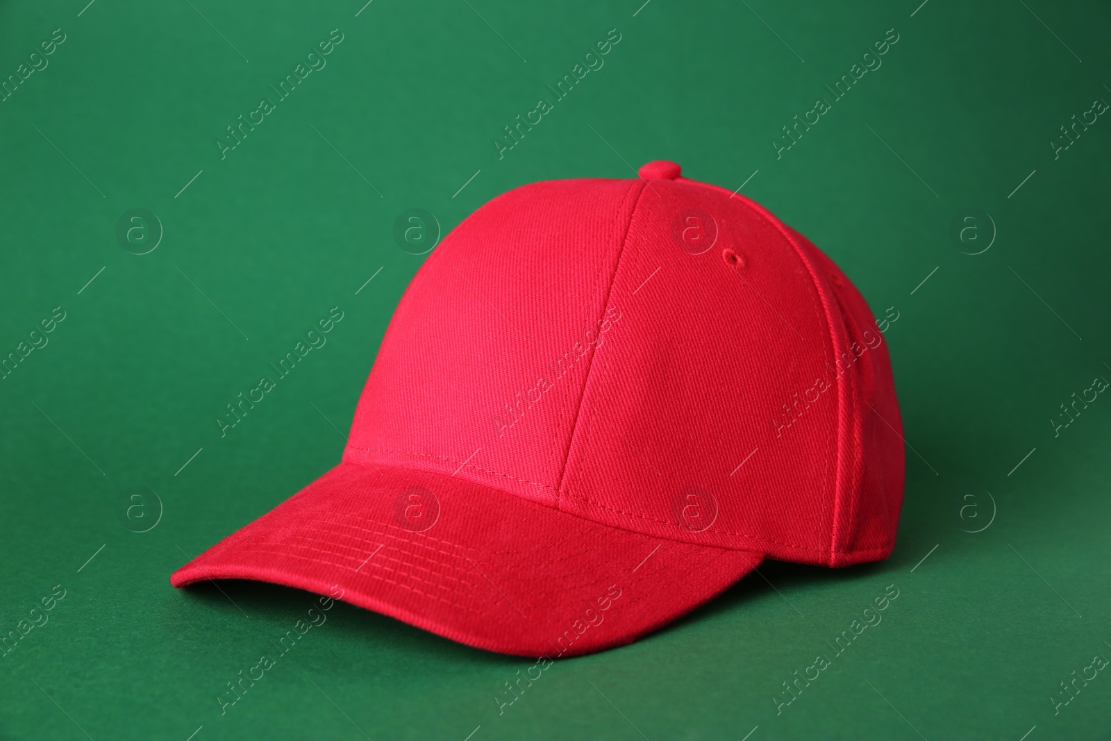 Photo of Stylish red baseball cap on green background