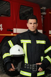 Photo of Portrait of firefighter in uniform with helmet near fire truck at station