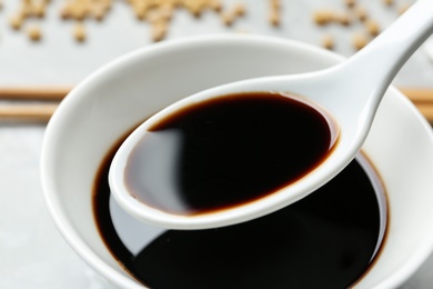 Spoon with soy sauce over bowl, closeup