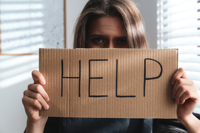 Photo of Abused young woman with sign HELP indoors. Domestic violence concept