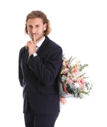 Young handsome man in stylish suit hiding beautiful flower bouquet behind his back on white background