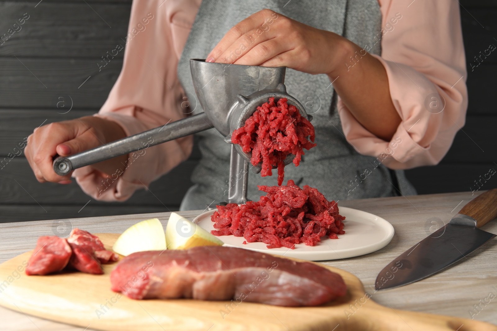 Photo of Woman making beef mince with manual meat grinder at light wooden table, closeup