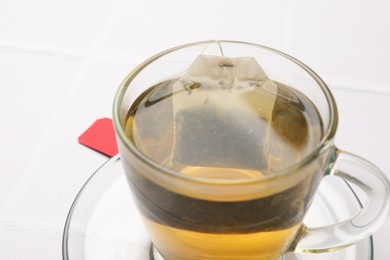 Photo of Tea bag in cup with hot drink on white table, closeup