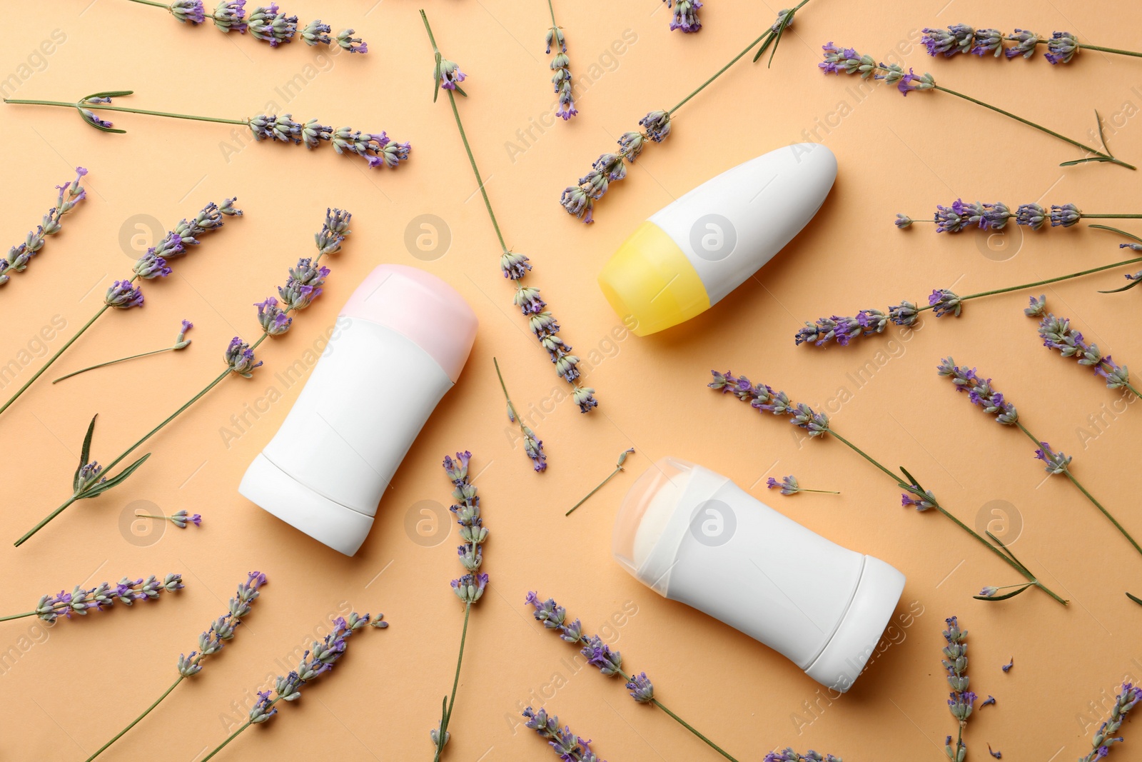 Photo of Different female deodorants and lavender flowers on apricot background, flat lay