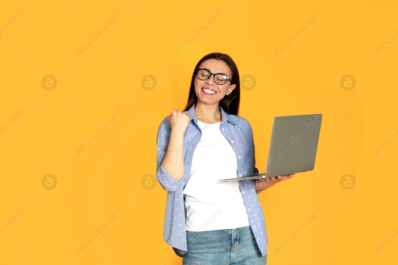 Photo of Young woman with modern laptop on yellow background