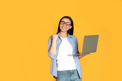 Photo of Young woman with modern laptop on yellow background