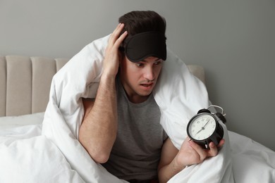 Emotional man with alarm clock in bed. Being late because of oversleeping