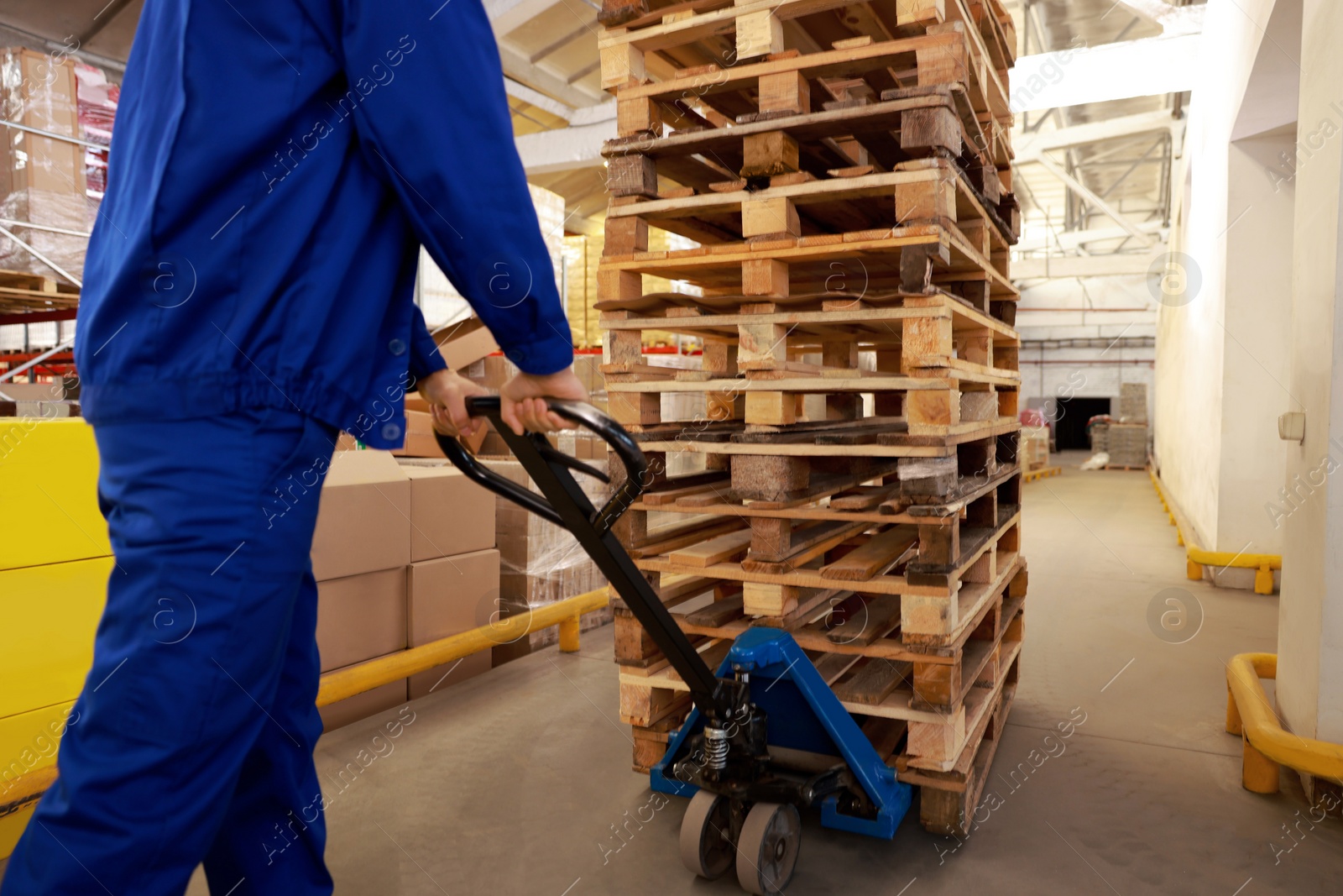 Image of Worker moving wooden pallets with manual forklift in warehouse, closeup