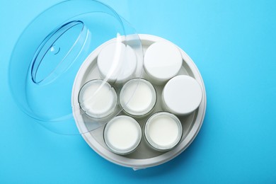 Modern yogurt maker with full jars on light blue background, top view