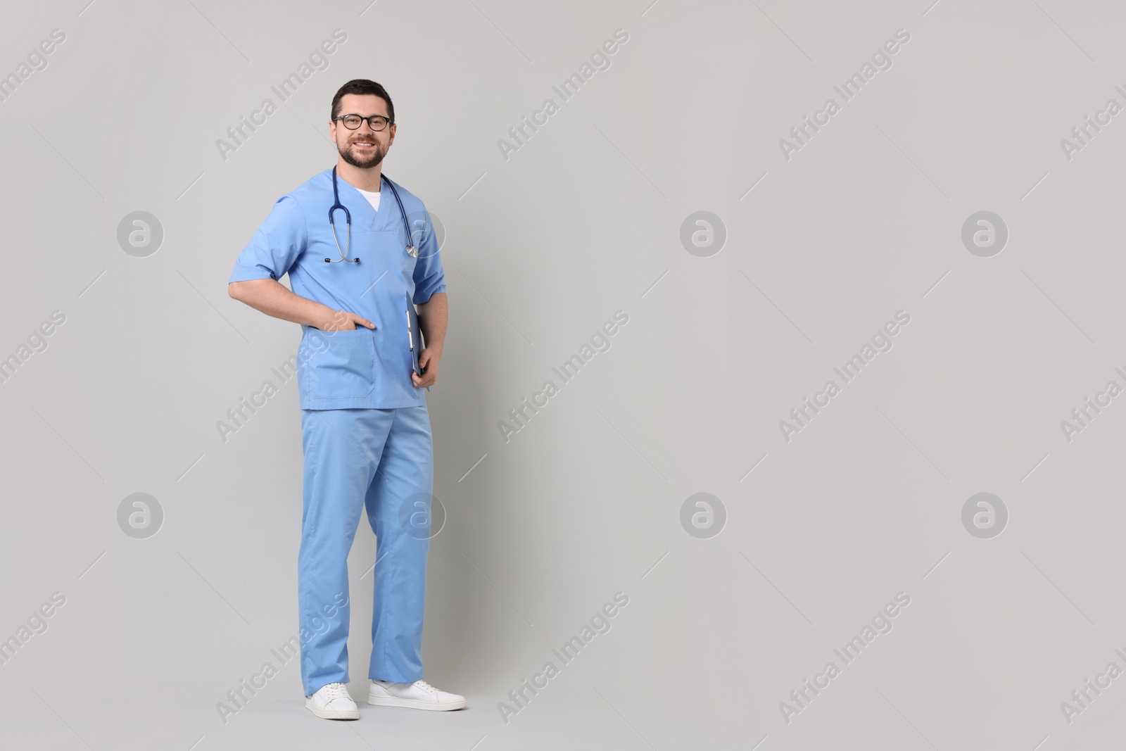 Photo of Full length portrait of smiling doctor on light grey background. Space for text