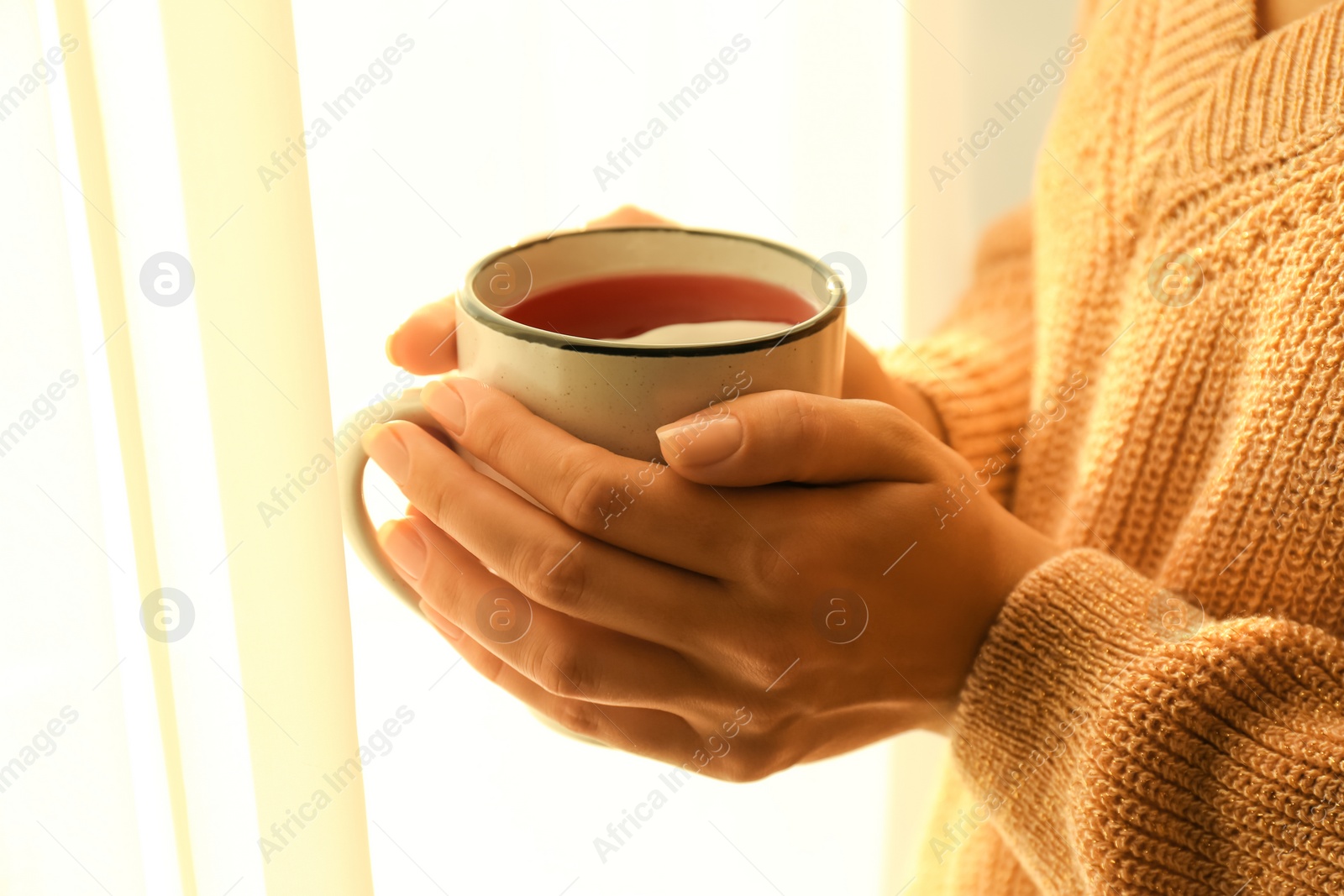 Photo of Woman holding elegant cup with tea near window indoors, closeup