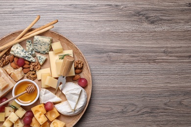 Photo of Cheese plate with honey, grapes and nuts on wooden table, top view. Space for text