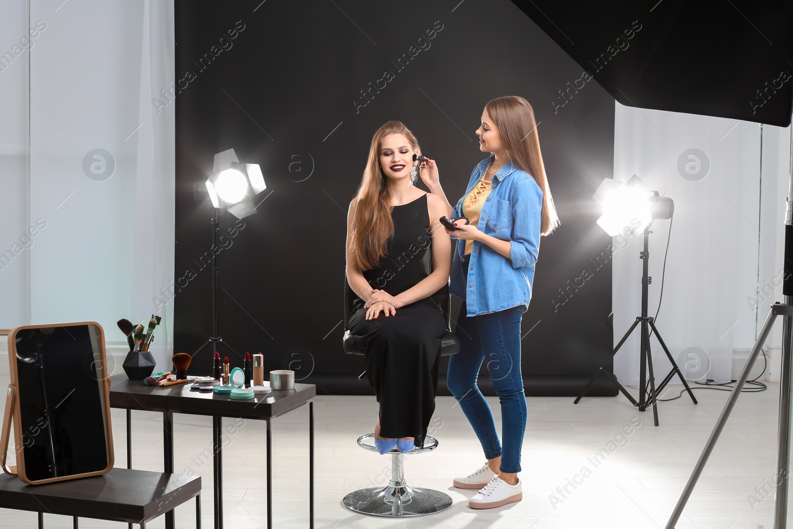 Photo of Professional makeup artist working with beautiful young woman in photo studio