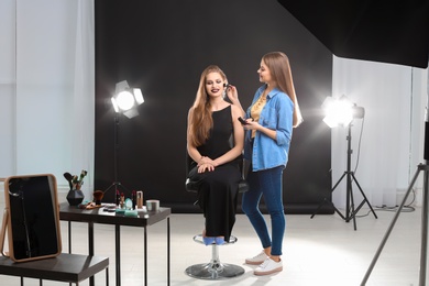 Professional makeup artist working with beautiful young woman in photo studio