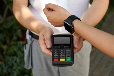 Photo of Woman using smartwatch for contactless payment outdoors, closeup