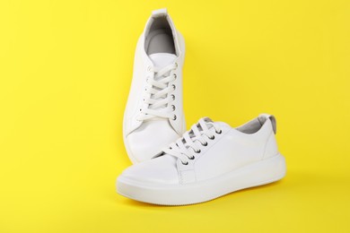 Photo of Pair of stylish white sneakers on yellow background