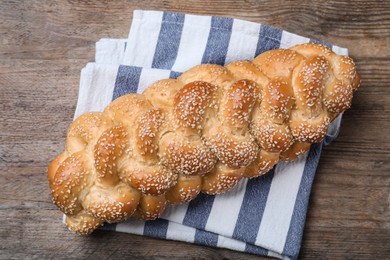 Photo of Homemade braided bread with sesame seeds on wooden table, top view. Traditional Shabbat challah