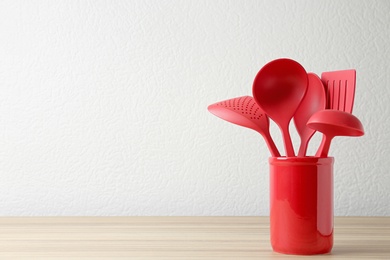Photo of Set of kitchen utensils in stand on wooden table near light wall. Space for text