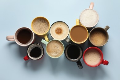 Many different cups with aromatic coffee on light blue table, flat lay