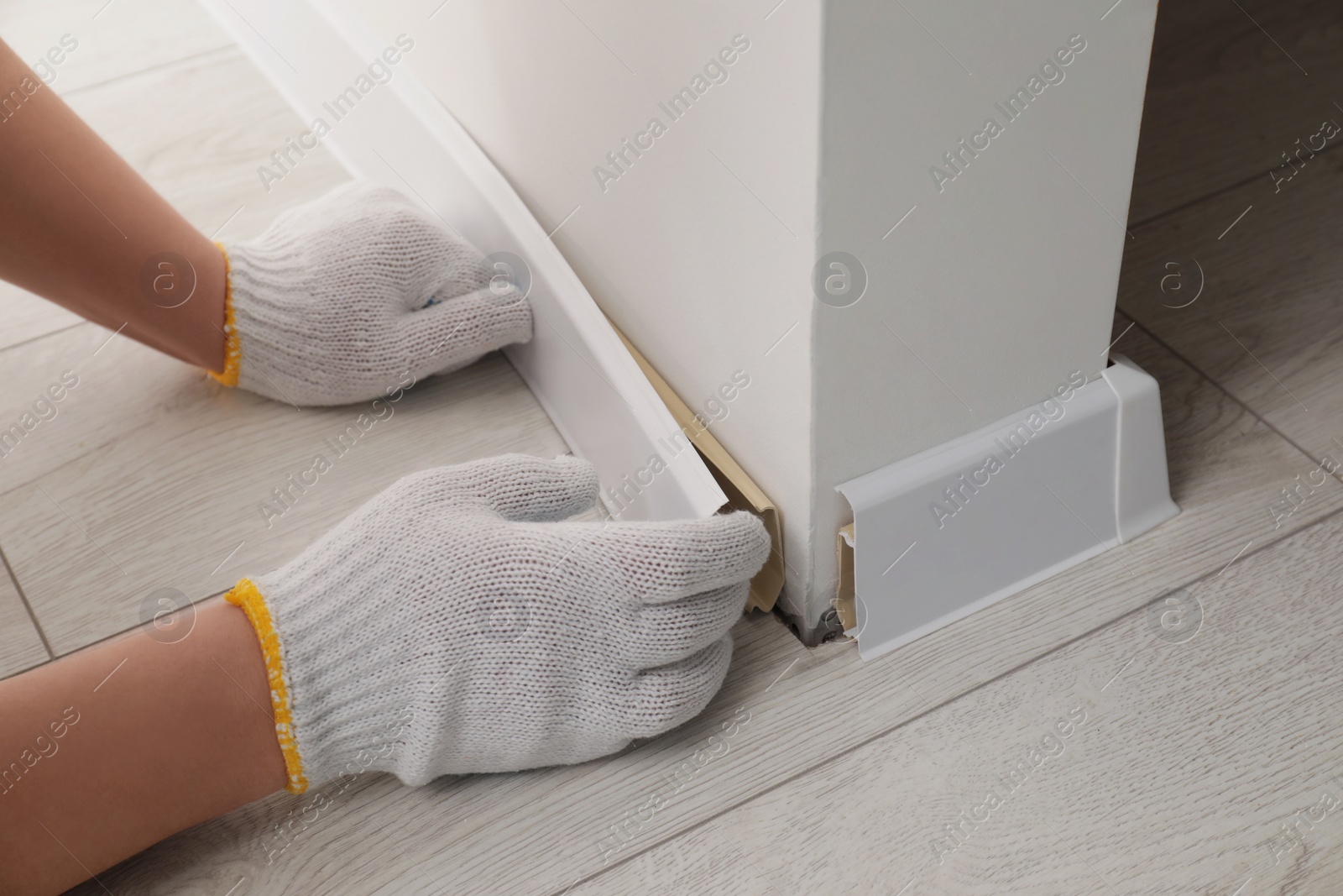 Photo of Man installing plinth on laminated floor in room, closeup