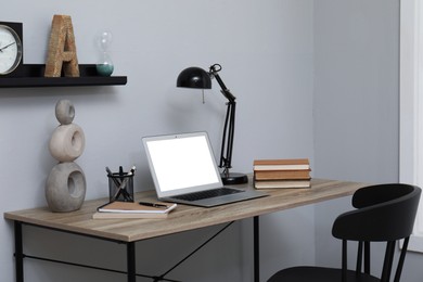 Photo of Comfortable workplace with modern laptop near light grey wall indoors