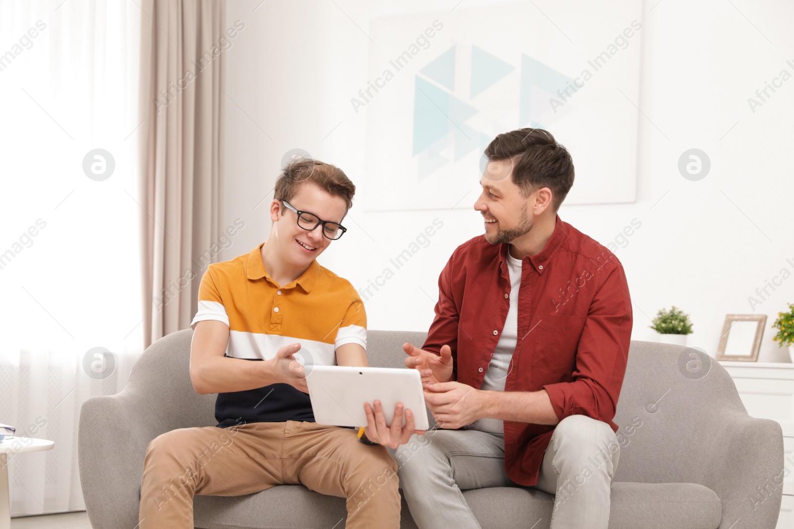 Photo of Happy father and his teenager son with tablet computer at home