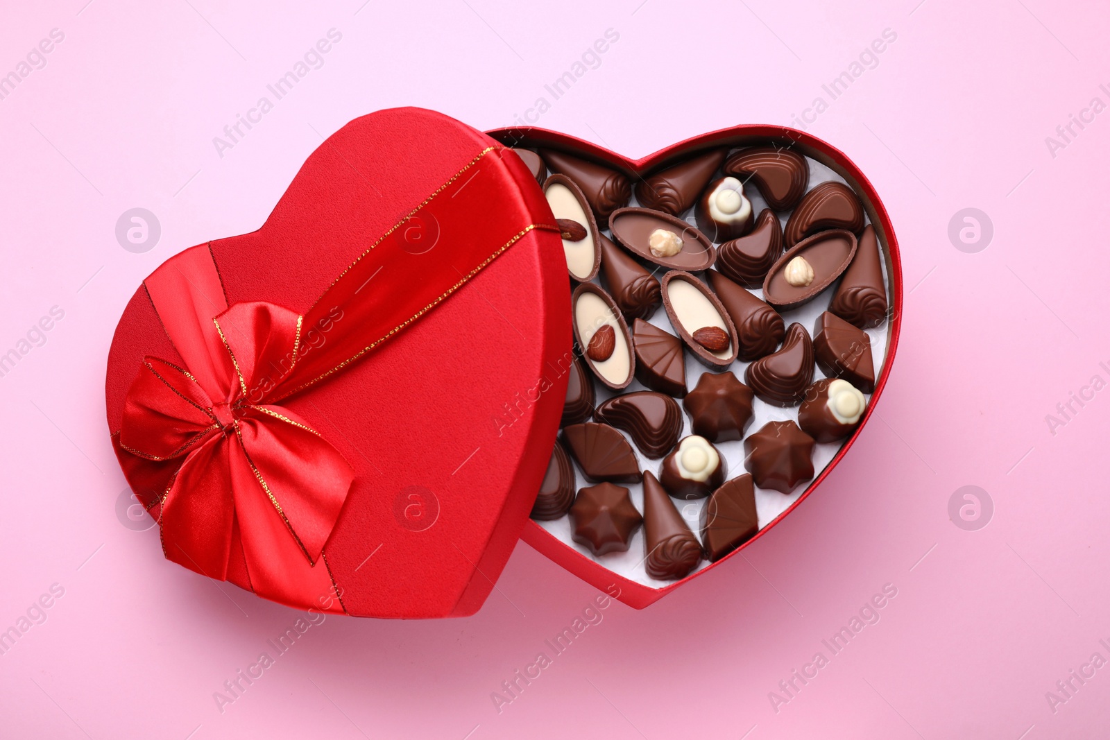 Photo of Heart shaped box with delicious chocolate candies on pink background, top view